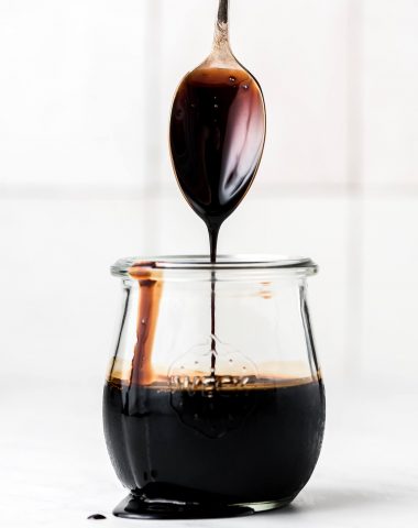 A spoon coated with balsamic glaze, lifted out a jar.