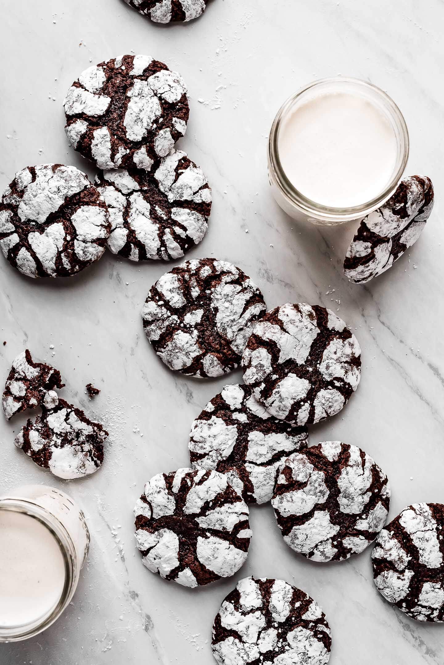 Chocolate Crinkle Cookies scattered on a marble surface with jars of milk.