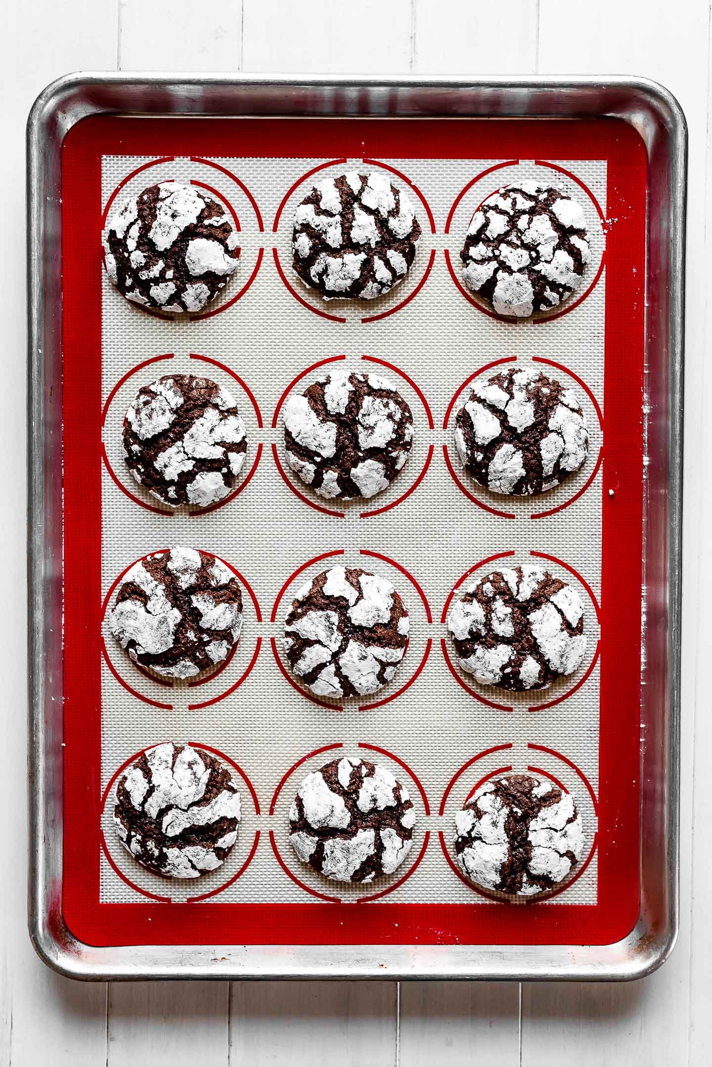 Chocolate Crinkle Cookies on a red silpat lined baking sheet.