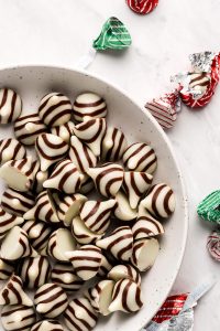 Unwrapped Hershey Hugs in a white bowl with wrapped ones scattered around.