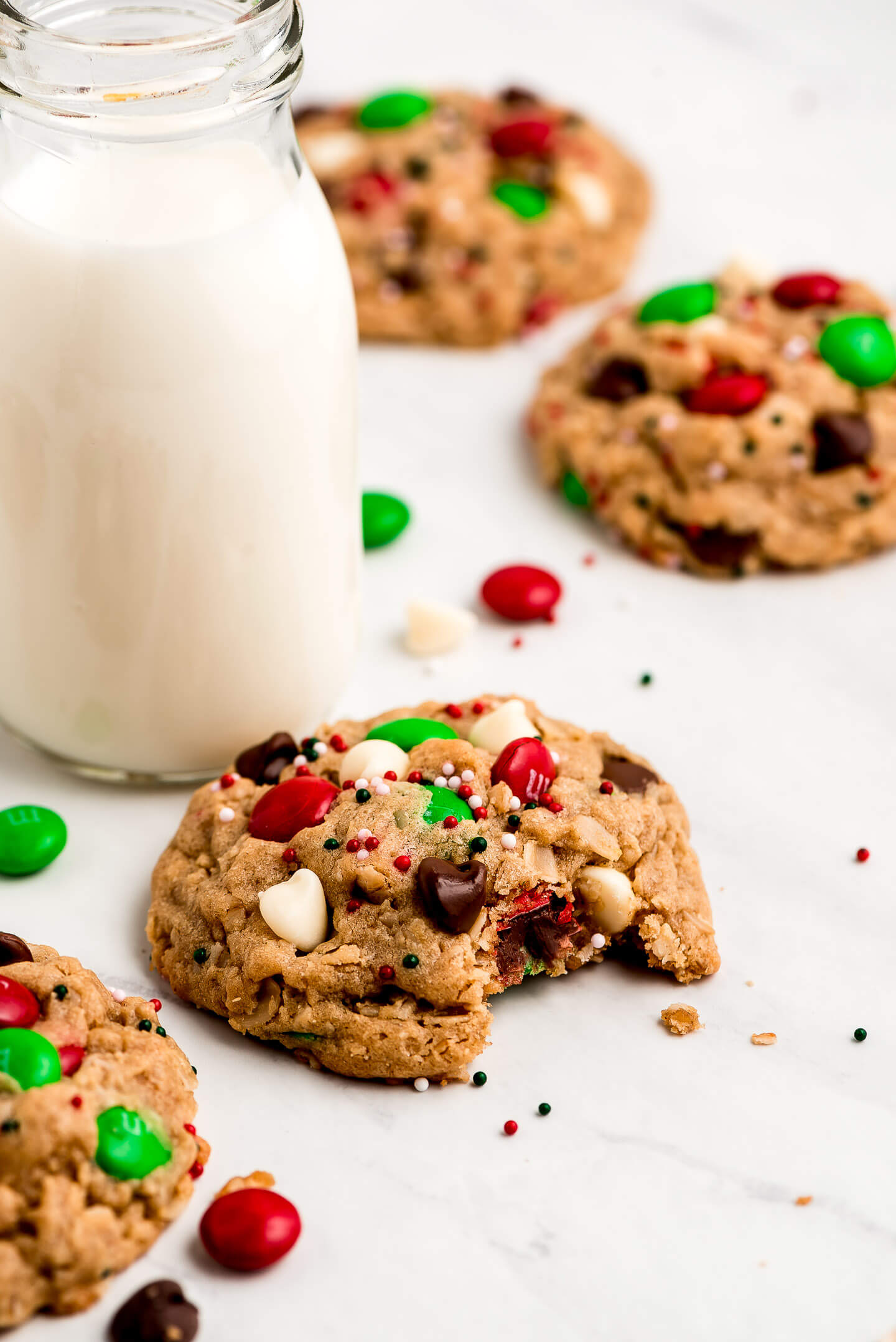 A Christmas Monster Cookie with a bite taken out and a jar of milk.