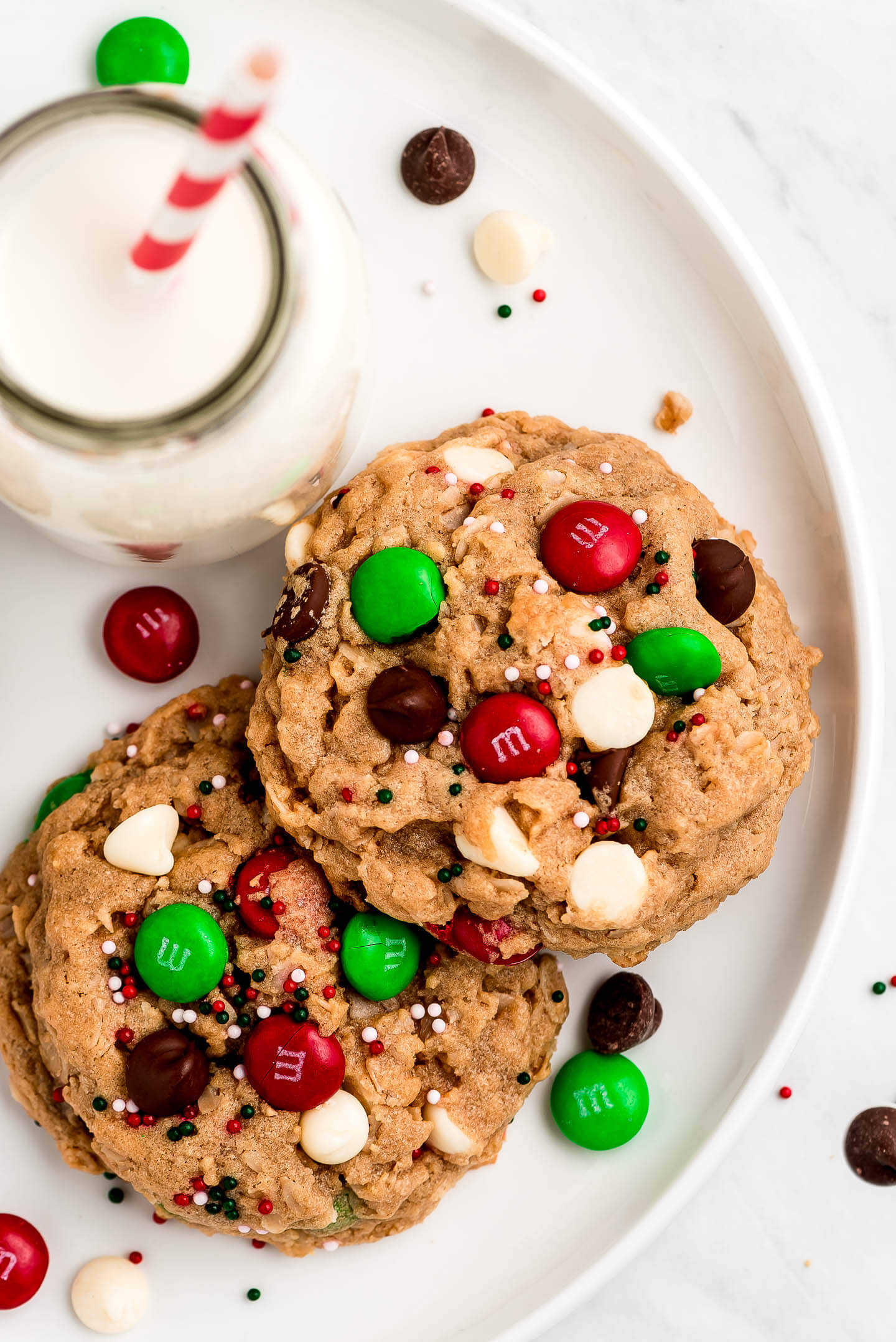 Cookies for Santa studded with M&M's and chocolate chips on a plate and a jar of milk.