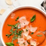 A bowl of Creamy Tomato Soup garnished with fresh basil and shaved parmesan.