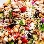Greek Couscous Salad with chicken in a large mixing bowl with spoons.