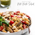 A serving bowl of pasta salad with chicken, tomatoes, mozzarella, and pesto.