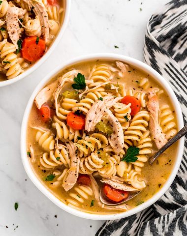 A large bowl of Rotisserie Chicken Noodle Soup with rotini noodles, shredded chicken, carrots, and parsley.