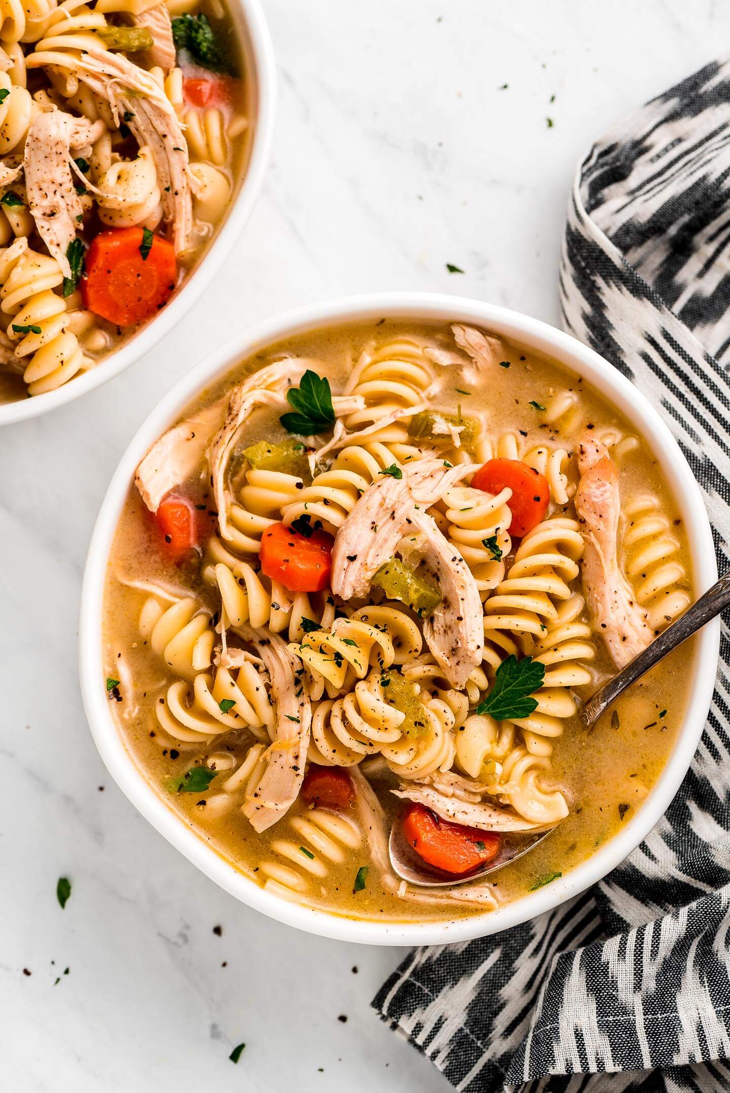 A large bowl of Rotisserie Chicken Noodle Soup with rotini noodles, shredded chicken, carrots, and parsley.