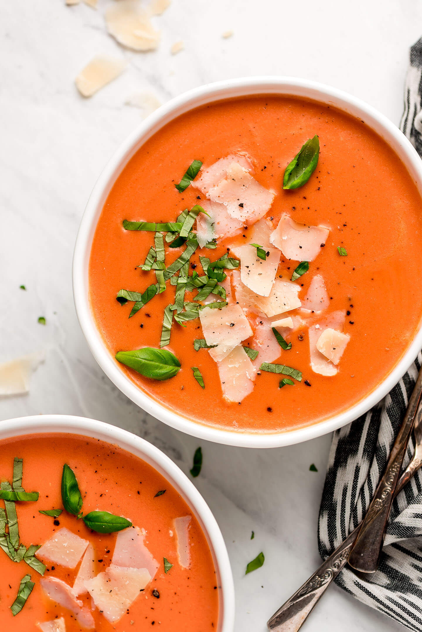 Two bowls of Creamy Tomato Soup garnished with basil and parmesan.