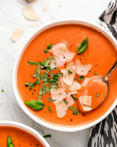 A bowl of Creamy Tomato Soup garnished with fresh basil and shaved Parmesan cheese.