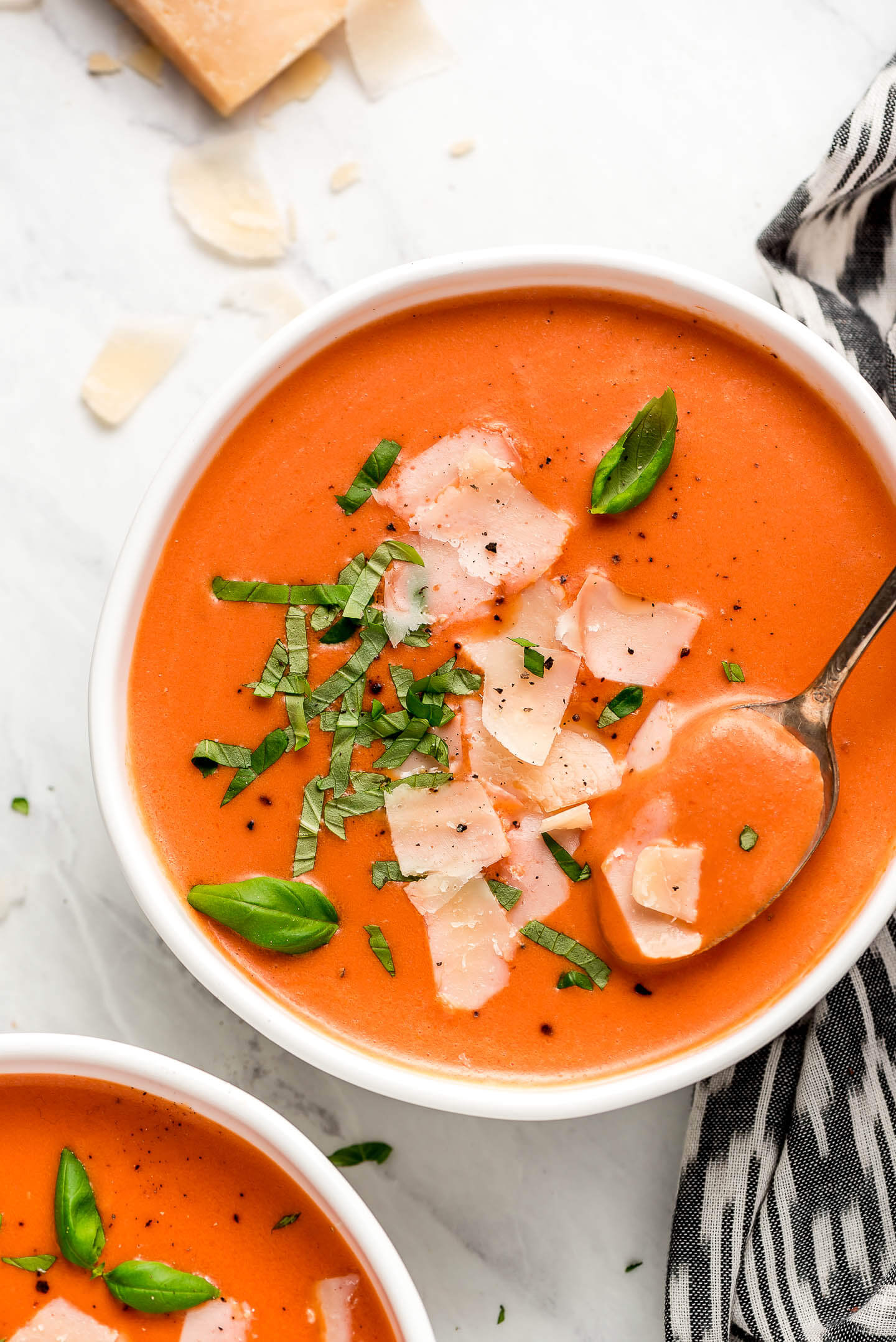 Creamy Tomato Basil Soup garnished with shaved parmesan, black pepper, and ribbons of basil.
