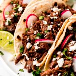 Beef Barbacoa in corn tortillas garnished with cilantro, sliced radishes, and queso fresco.