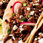 Beef Barbacoa in corn tortillas garnished with cilantro, sliced radishes, and queso fresco.