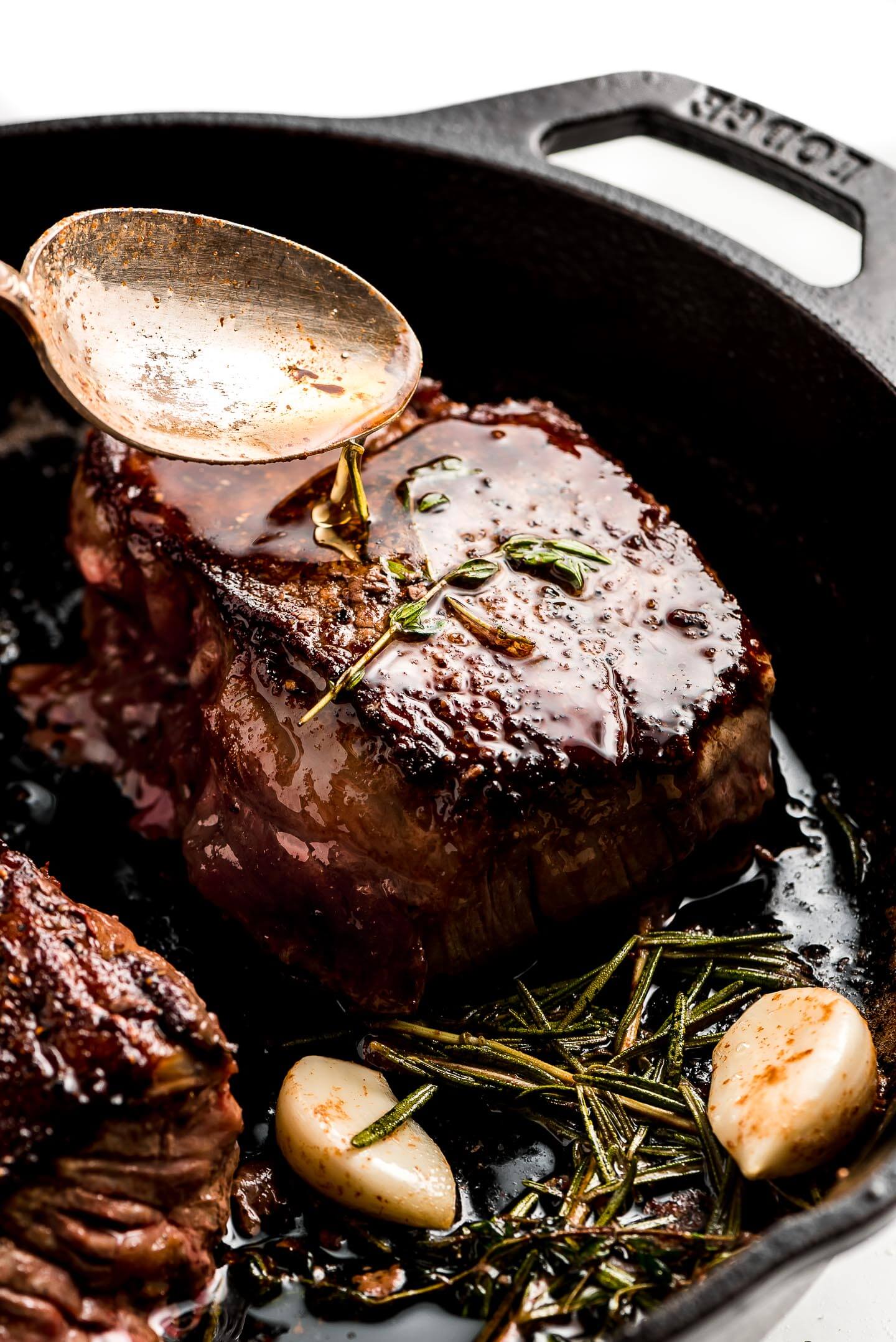 Spooning melted butter over a filet mignon in a cast iron skillet.