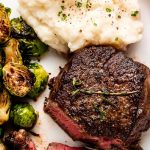A plate of mashed potatoes, brussels spouts, and filet mignon with a few bites cut off.