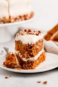 A slice of Moist Easy Carrot Cake on a plate with a fork full on the side.