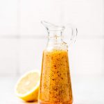 Homemade Italian Dressing in a glass bottle with a spout and handle and a lemon in the background.
