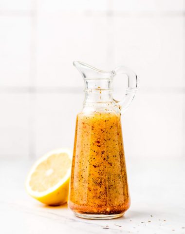 Homemade Italian Dressing in a glass bottle with a spout and handle and a lemon in the background.
