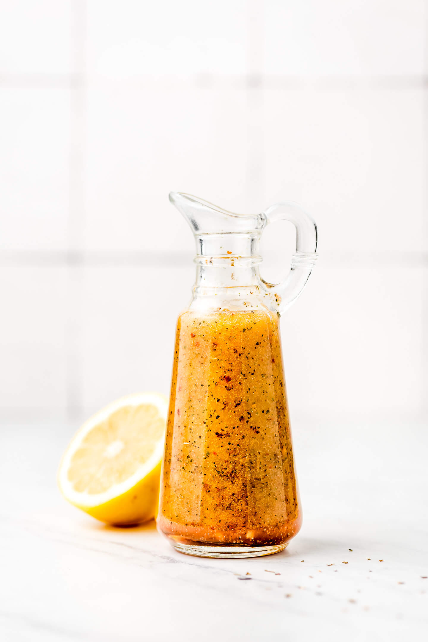 Homemade Italian Dressing in a glass bottle with a spout and handle and a lemon in the background.