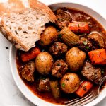 A bowl of Instant Pot Beef Stew with a slice of artisan bread on the side.
