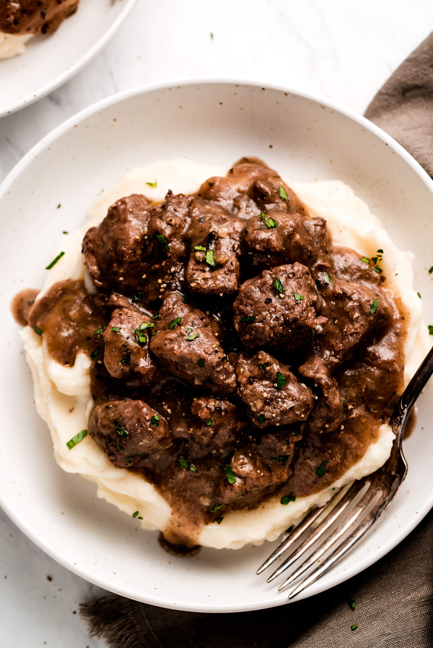 A bowl of Beef Tips and Gravy over mashed potatoes and garnished with fresh parsley.