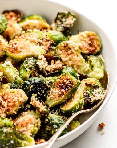 Parmesan Brussels Sprouts in a white serving bowl with a spoon in the side.