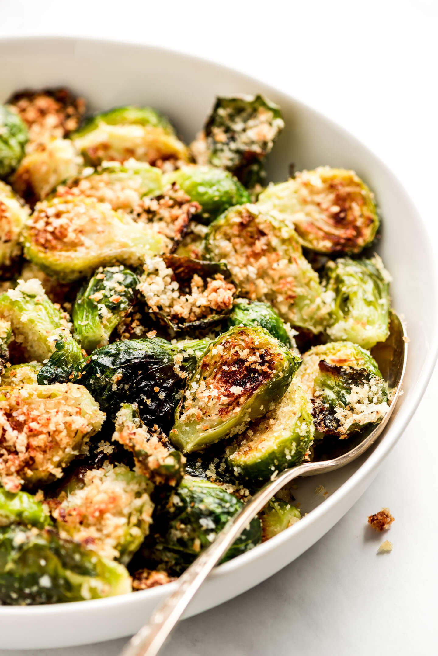 Parmesan Brussels Sprouts in a white serving bowl with a spoon in the side.