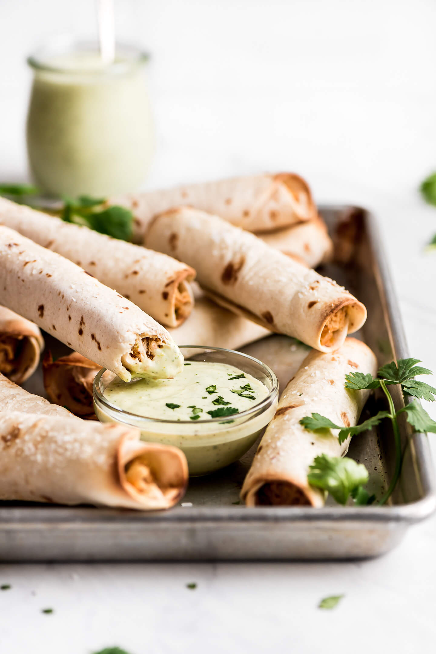 A taquitos resting on the side of a bowl of creamy cilantro lime dip.