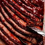 Tongs grabbing slices of barbecue Brisket from a pan.