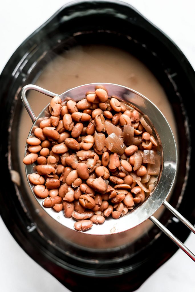 A strainer full of cooked pinto beans held over a slow cooker.