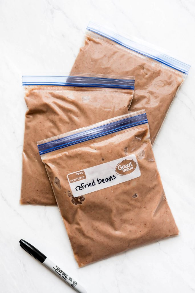 Slow Cooker Refried Beans in freezer plastic bags on a marble surface.
