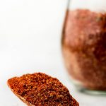A heaping spoonful of Taco Seasoning on marble with jar of it blurred in the background.