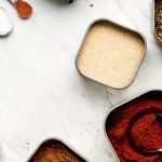 Various tins of spices and measuring spoons on a marble surface.