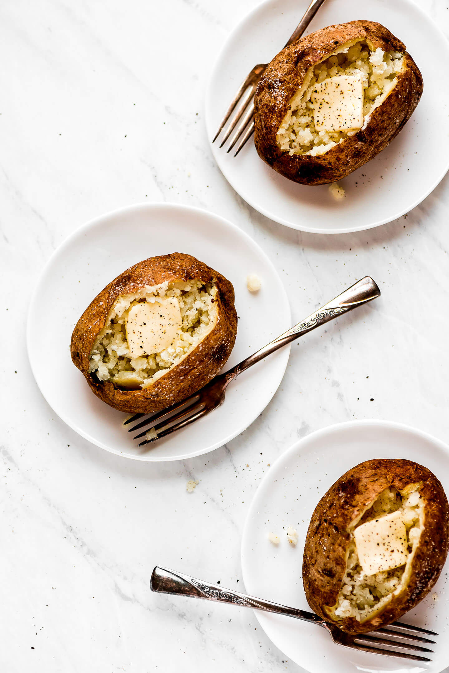 Three fluffed and buttered baked potatoes on plates.