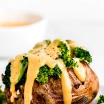 Cheese sauce dripping down a baked potato topped with broccoli.