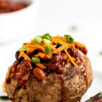 A baked potato topped with chili, cheese, and green onions.