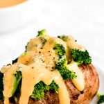 Cheese sauce dripping down a baked potato topped with broccoli.