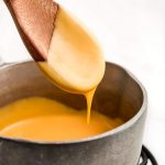 A wooden spoon with cheese sauce on it and dripping down into a pot.