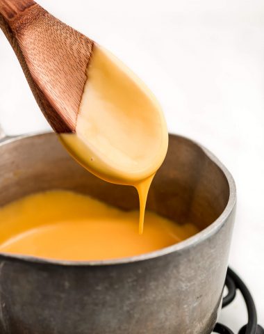 A wooden spoon with cheese sauce on it and dripping down into a pot.