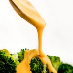 Spooning Cheese Sauce over steamed broccoli.