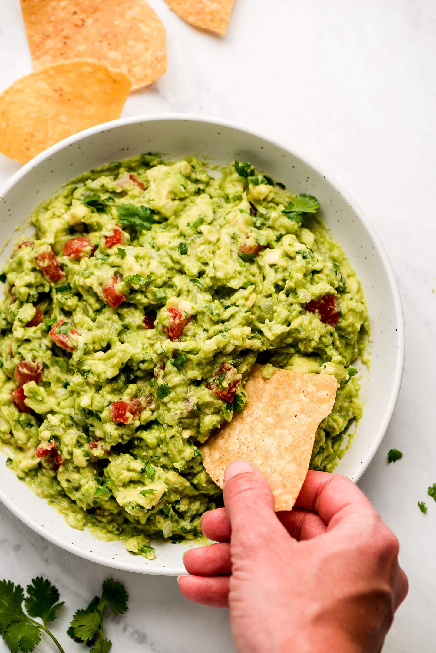 A hand dipping a chip in a large bowl of guacamole.