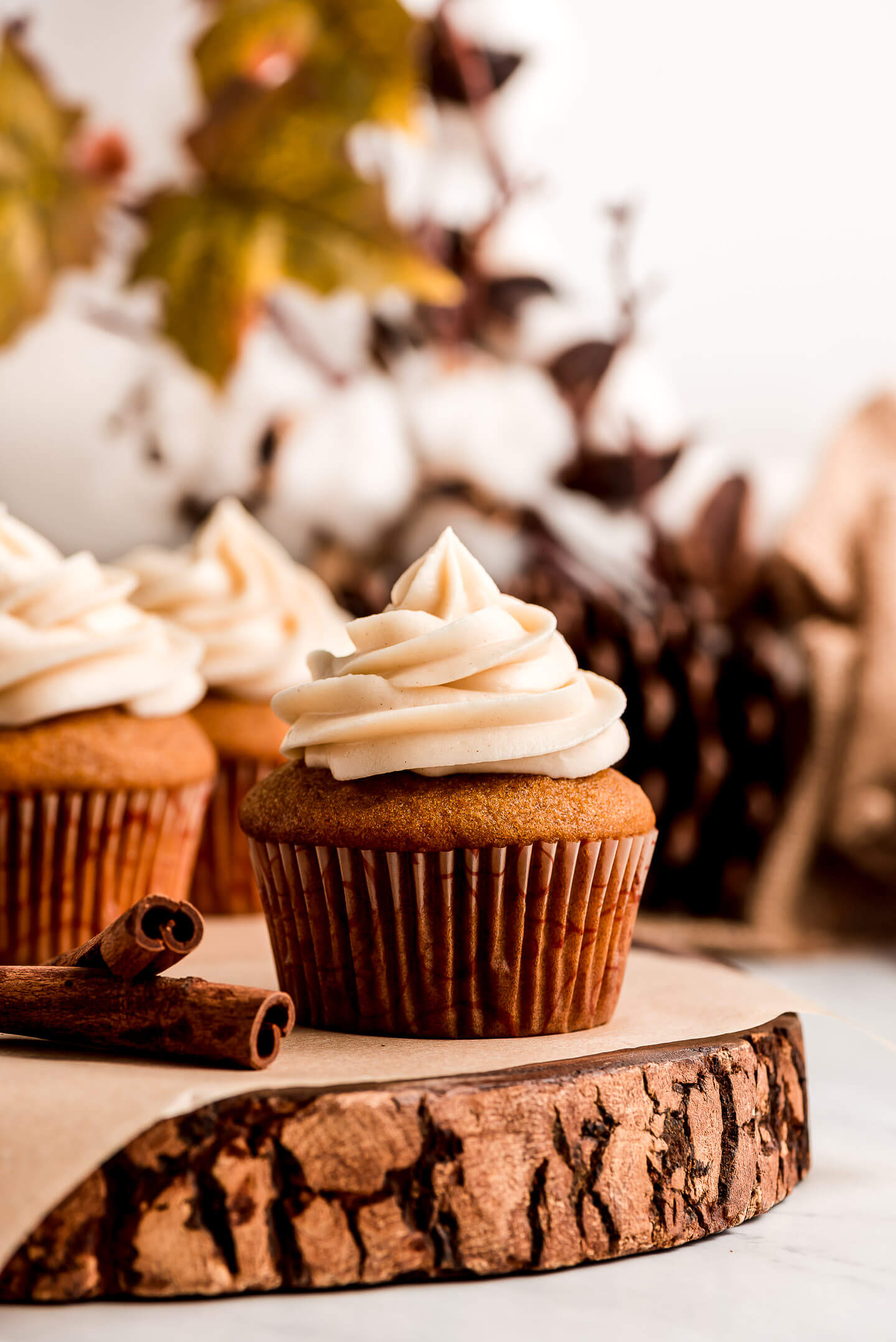 A Pumpkin Cupcake topped with cinnamon Cream Cheese Frosting on a wood slice cake stand.