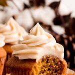 A Pumpkin Cupcake topped with cinnamon Cream Cheese Frosting with a bite taken out.