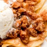 A close up shot of apple crumble in a bowl with ice cream on top starting to melt.