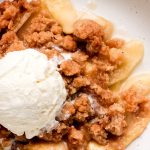 A close up shot of apple crumble in a bowl with ice cream on top starting to melt.