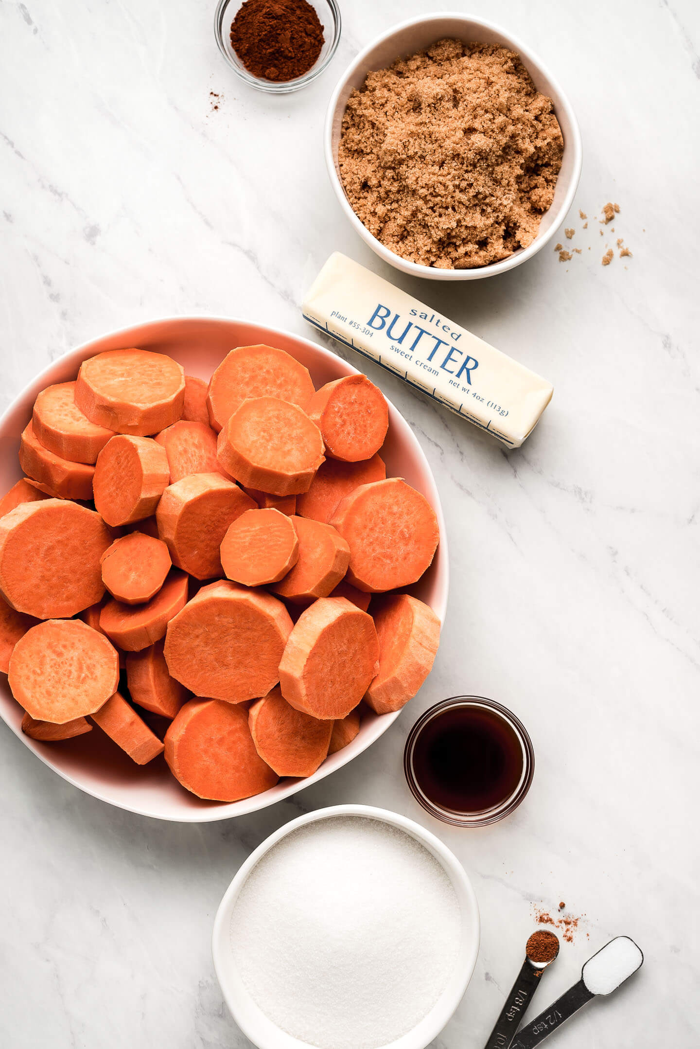 Ingredients on a marble surface- cinnamon, brown sugar, butter, sweet potatoes, vanilla extract, granulated sugar, nutmeg, and salt.