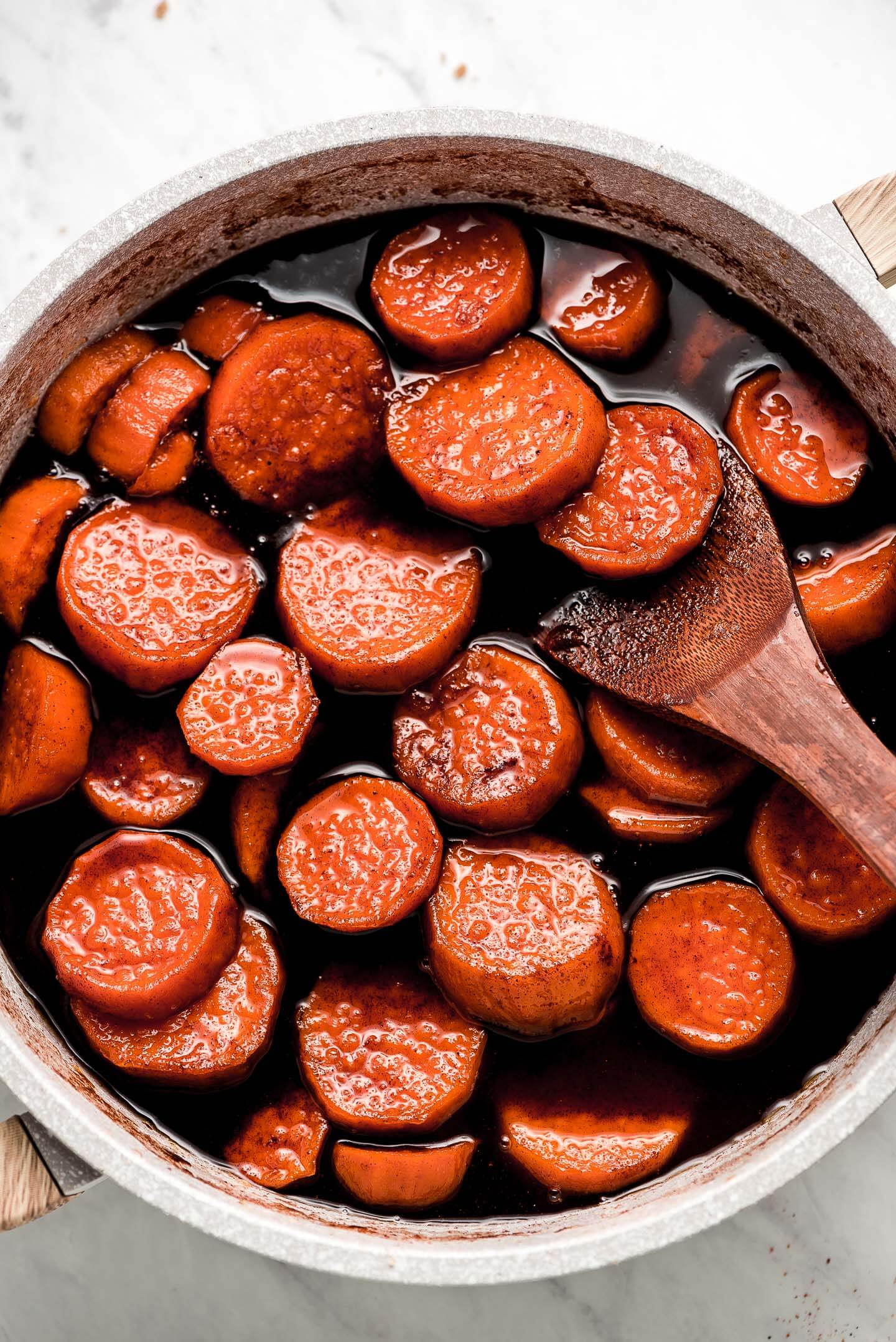 Candied Yams in a large pan with a wooden spoon lifting some out.