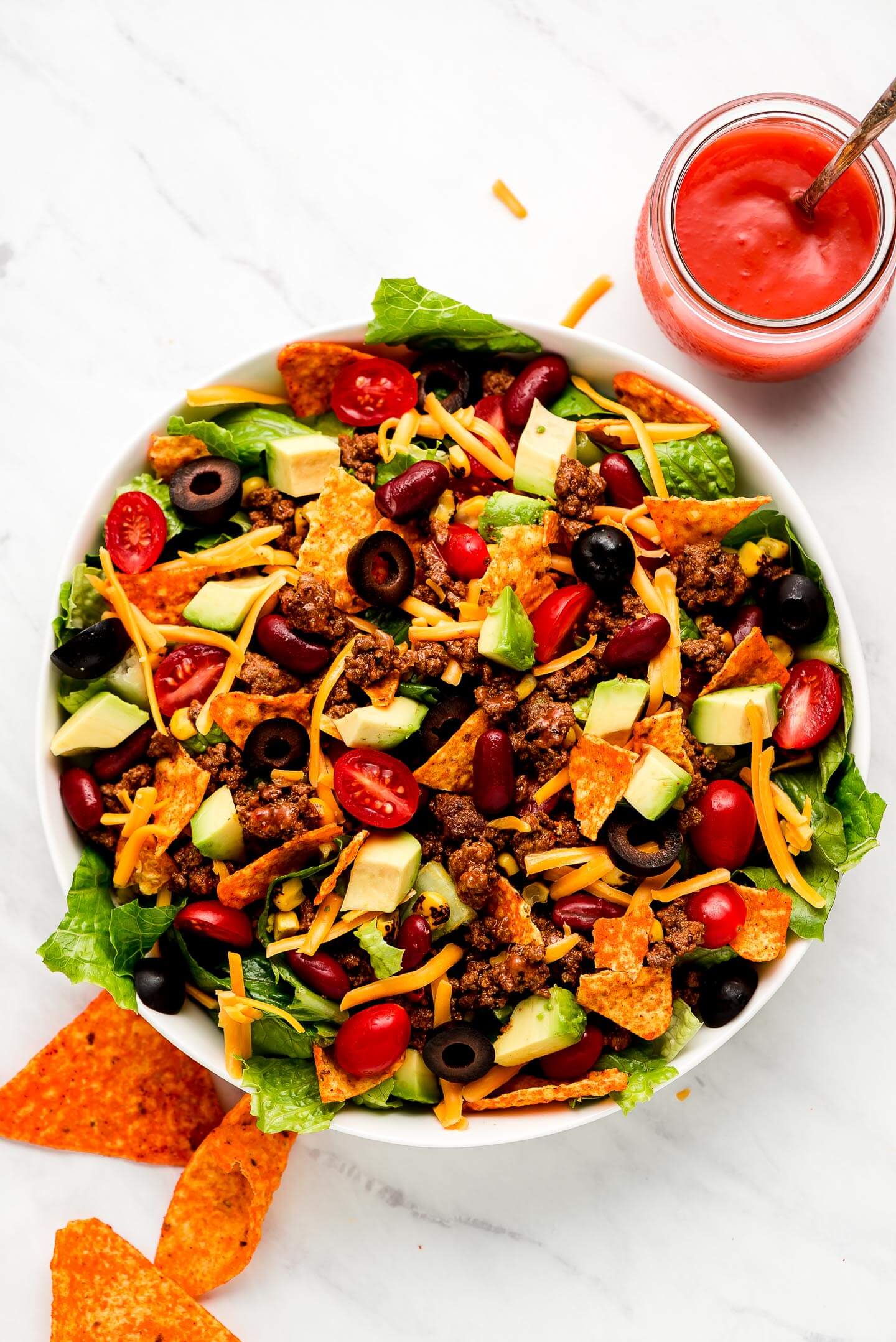 A large bowl full of Dorito Taco Salad with a jar of Catalina dressing to the side.