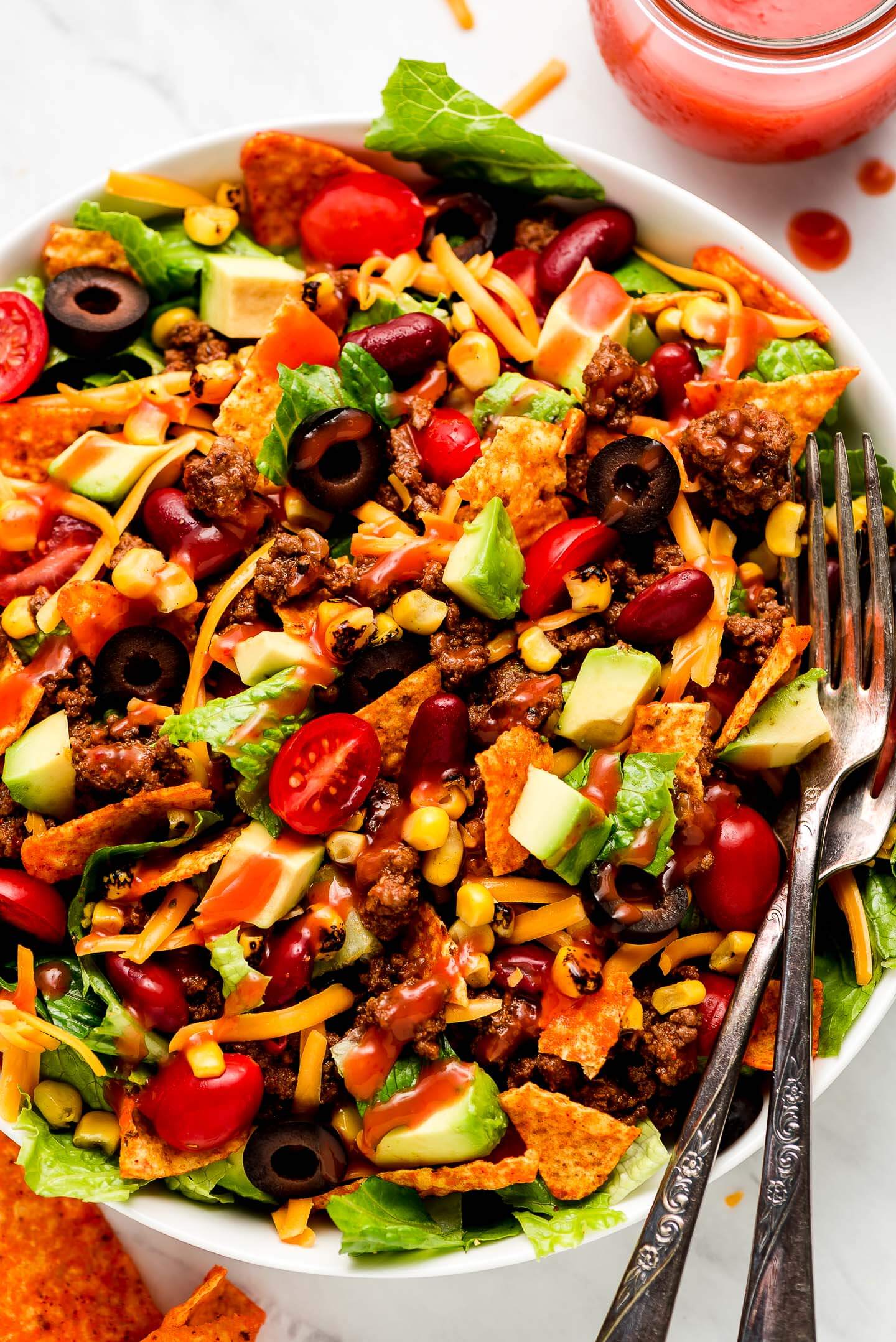 Close up shot of Dorito Taco Salad drizzled with Catalina dressing and two forks in the side.