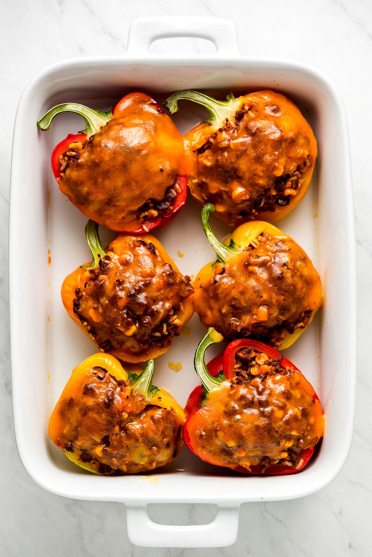 Halved Stuffed Bell Peppers topped with melted cheese in a 9x13 pan.