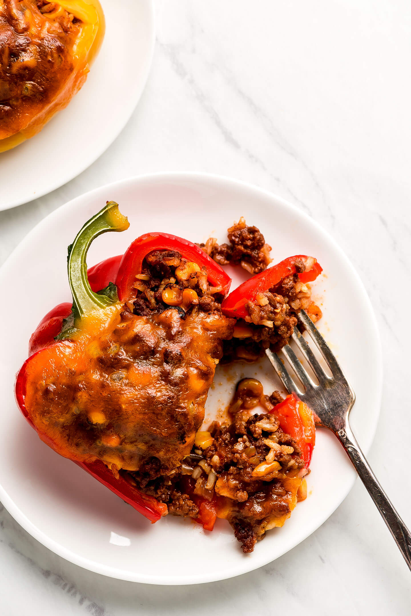 A stuffed red bell pepper on a plate with a few pieces cut off with a fork on the side.